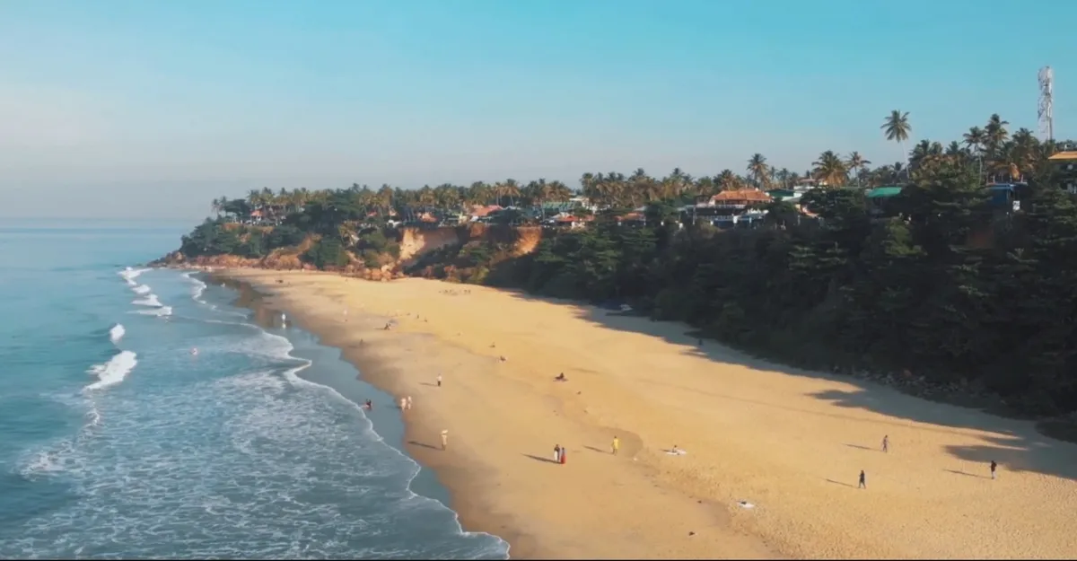 A lively day at Varkala Beach, Kerala, where people relax on the sand with a beautiful hill visible in the distance.