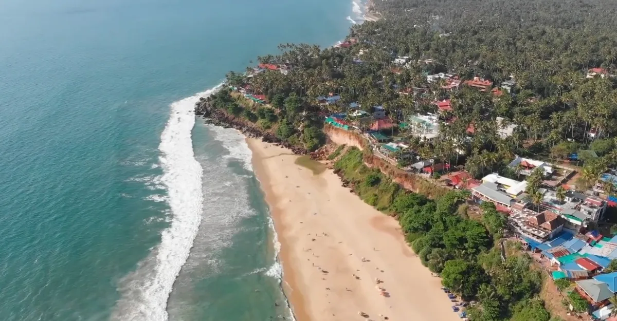 Aerial view of a tropical beach with waves, sandy shore, and adjacent greenery.