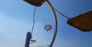 Parasailing adventure at Anjuna Beach, Goa, with a colorful parachute soaring in the clear blue sky, viewed from under the shade of a beach umbrella.