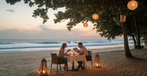 Romantic beachside dinner at sunset with a couple under lantern-lit tree, ocean waves in the background