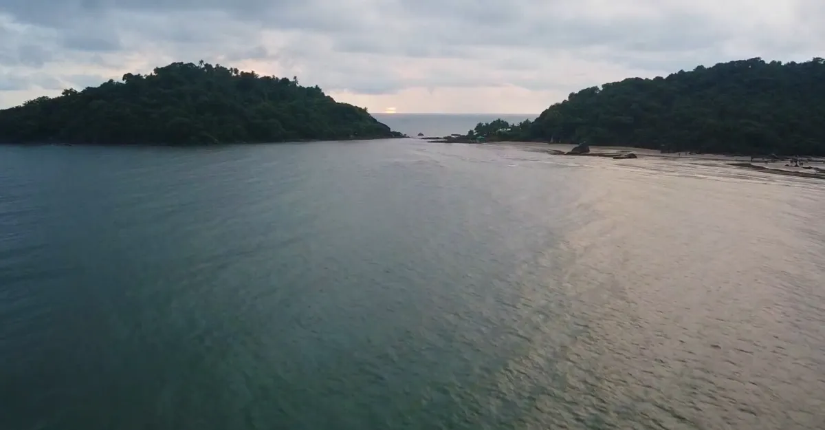 Aerial view of a serene body of water flanked by two lush, forested landmasses under an overcast sky.