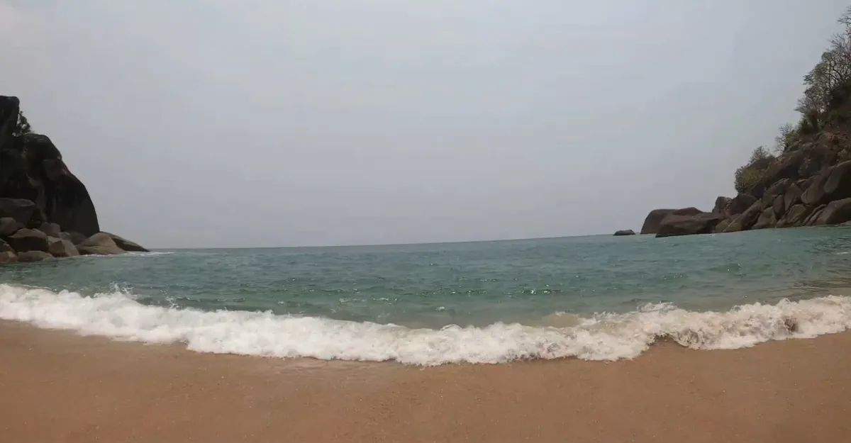 Calm waves on golden sands at Butterfly Beach Goa, framed by rocky cliffs and clear skies, a serene retreat perfect for peaceful getaways.